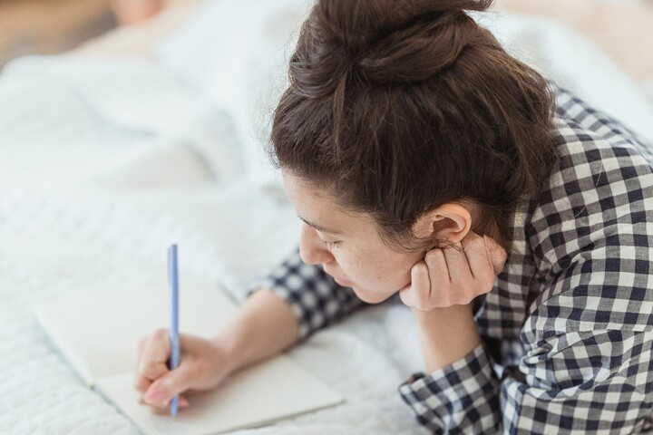 Person writing while lying on a bed