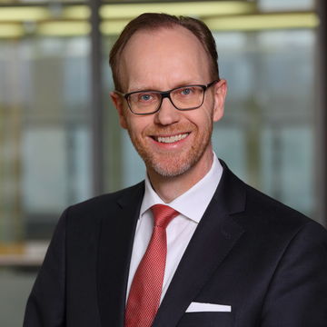Portrait von Henning Lobin. Er trägt ein weißes Hemd, eine rote Krawatte sowie einen schwarzenn Blazer und lächelt.