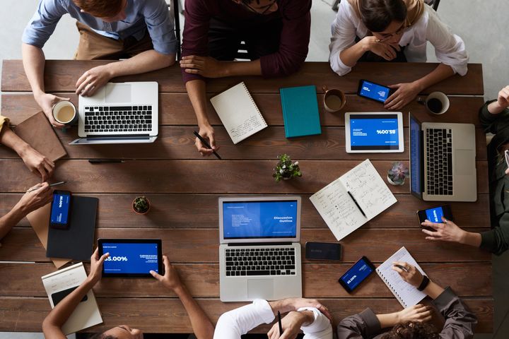 mehrere Personen, die mit einem Laptop an einem Tisch arbeiten